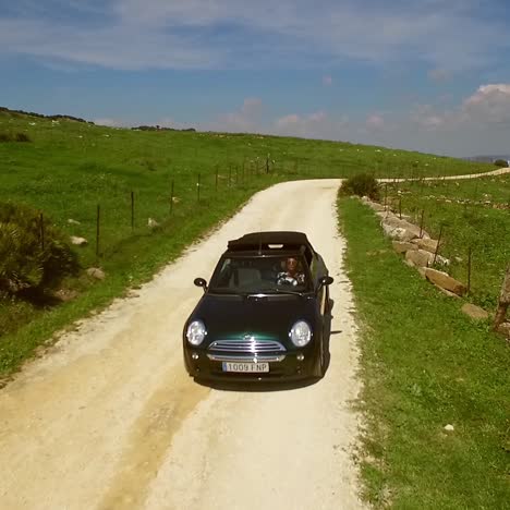 mujer joven conduciendo un cabriolet en un camino de tierra