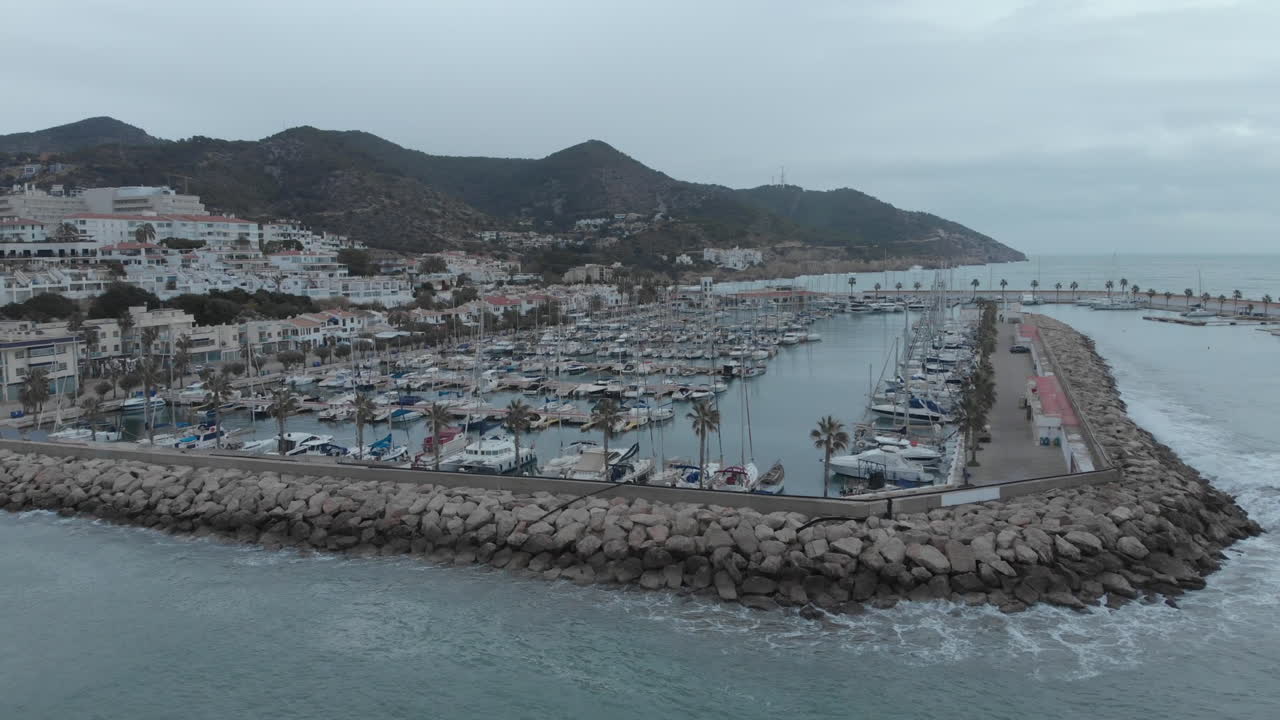 una toma aérea de un dron captura los muelles con yates, un pueblo costero y montañas en el fondo