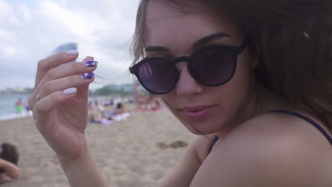 hermosa chica con gafas de sol sentada en la playa. mujer con el cabello ondeando en el viento