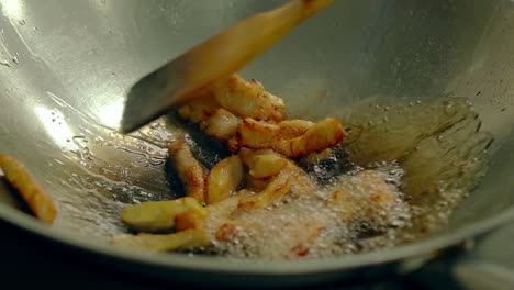 close up cooking fried potatoes in oil pan mixes them by wooden spatula