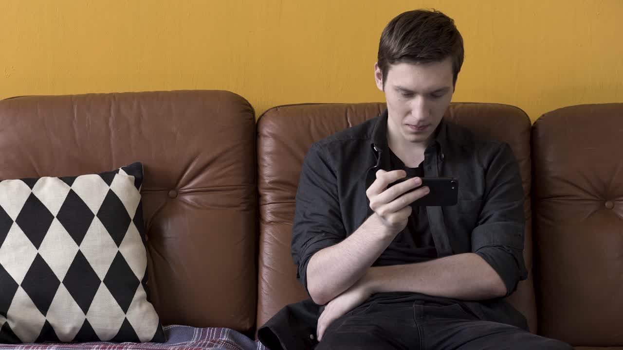 소파 에 스마트폰 을 사용하는 젊은 남자
