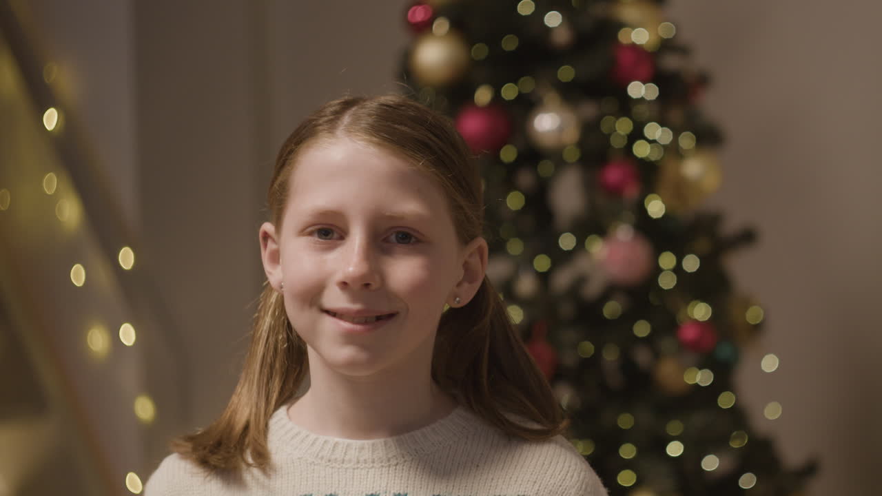 A girl poses in front of a Christmas tree