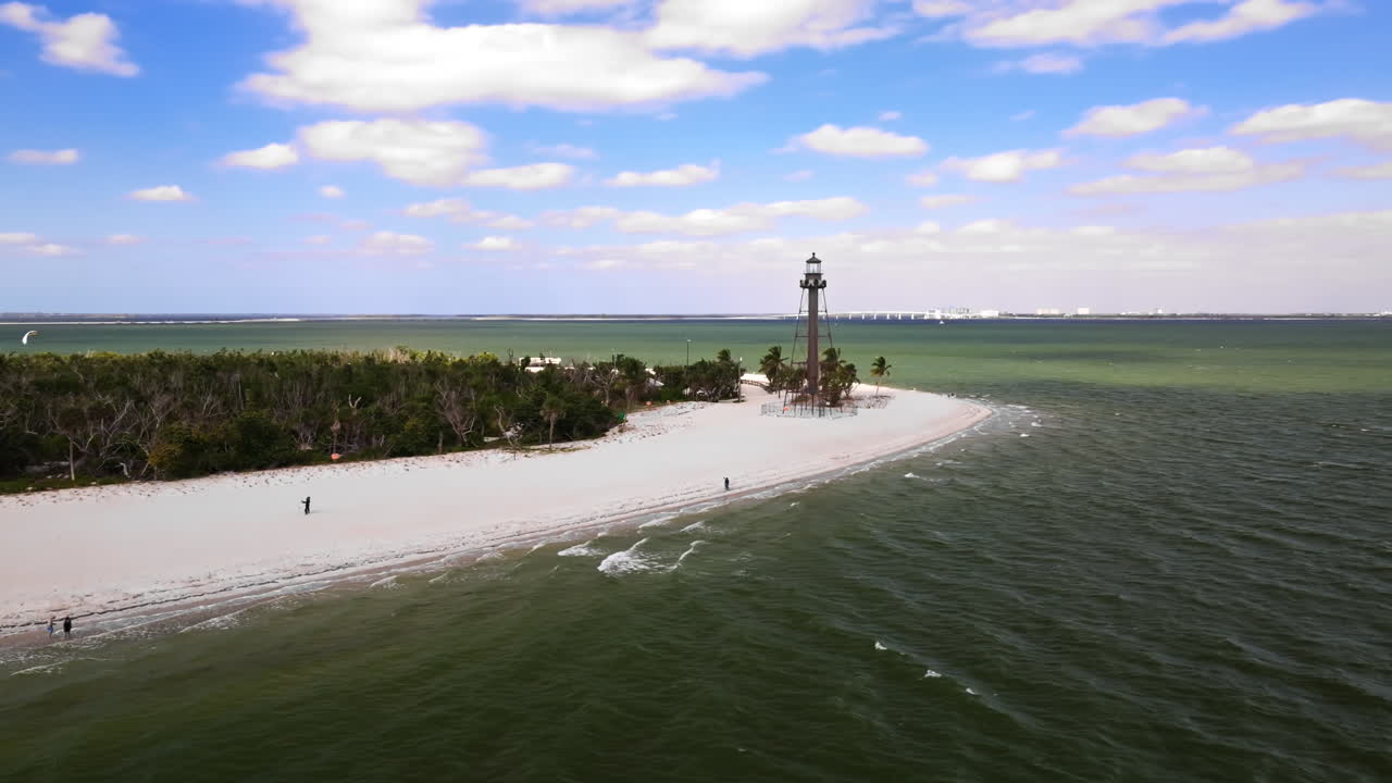 En filmisk vidvinkel droneoptagelse, der kredser om det historiske Sanibel Island Fyr ved den østlige ende af Sanibel Island, Florida, med lys kystlinje nær Fort Myers