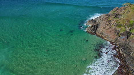 Vista-Lejana-De-Los-Turistas-Surfeando-En-La-Playa-Cerca-Del-Promontorio-Rocoso-De-Norries-En-Nueva-Gales-Del-Sur,-Australia