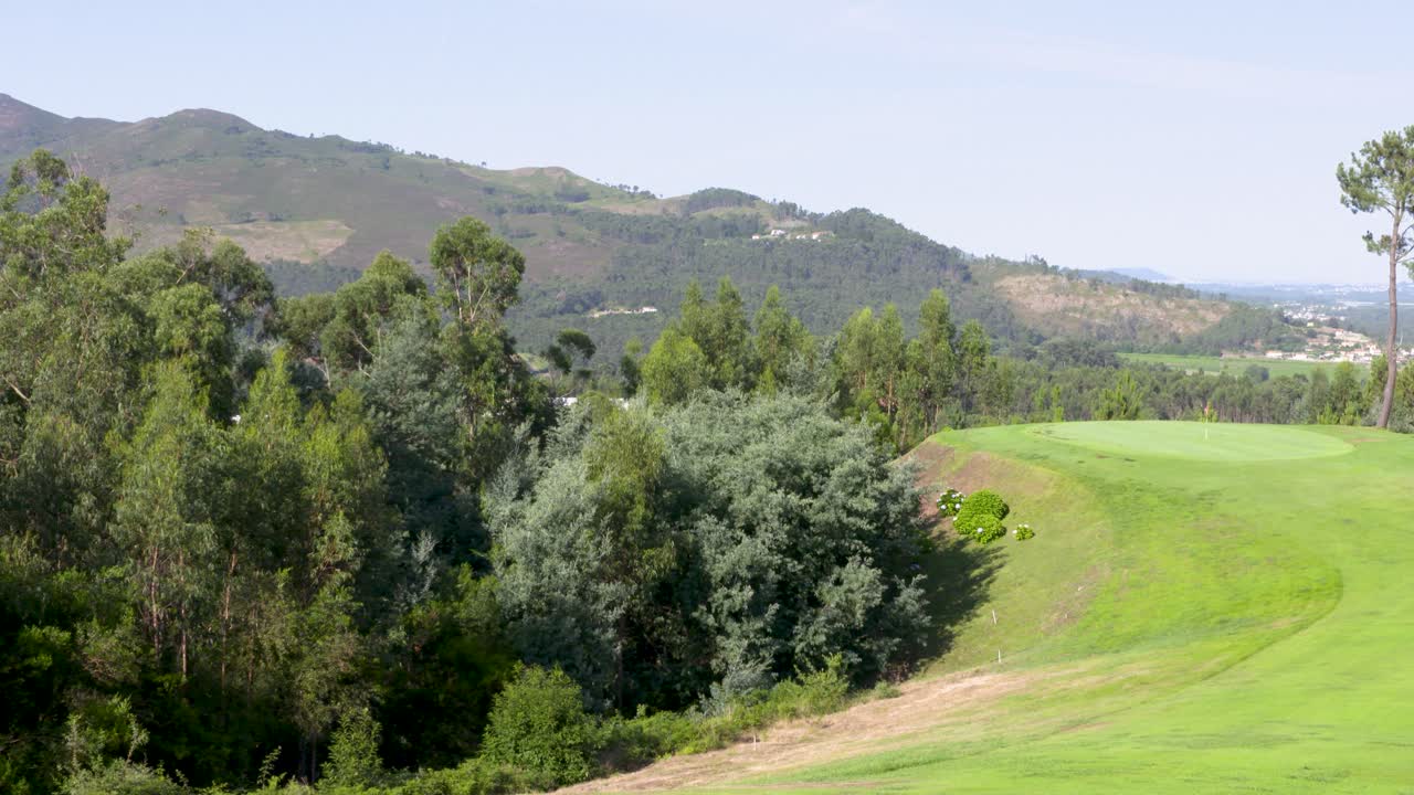 Panoramic view over the short green grass of the golf course with mountains and a valley in the background