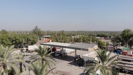 Vuelo-Aéreo-Sobre-Palmeras-Al-Lado-De-La-Gasolinera-Al-Lado-De-La-Carretera-En-Khairpur