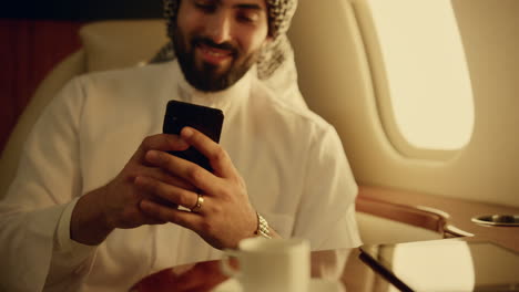 Smiling man texting message in airplane. Closeup hands holding smartphone in jet