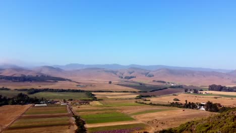 Drone-shot-over-farm-with-hills-and-blue-sky-in-the-background