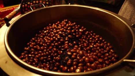 Slow-motion-footage-of-a-street-vendor's-huge-vat-of-fresh-roasted-chestnuts-at-a-nighttime-Thai-market