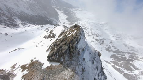 Racing-drone-flying-over-rocky-mountains-covered-with-snow-and-descending-toward-valley,-Pyrenees