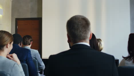 rear view of people sitting in a conference room who are listening to a caucasian businesswoman talking confidently and emotionally