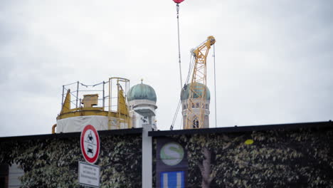 the iconic green domes of frauenkirche in munich rise above a construction site with cranes and scaffolding in the foreground. a contrast between historic architecture and modern urban development.