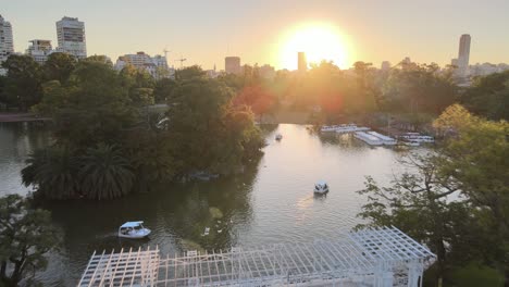 aerial dolly out of rosedal gardens pond with white bridge and palermo woods pedestrian street at sunset, buenos aires