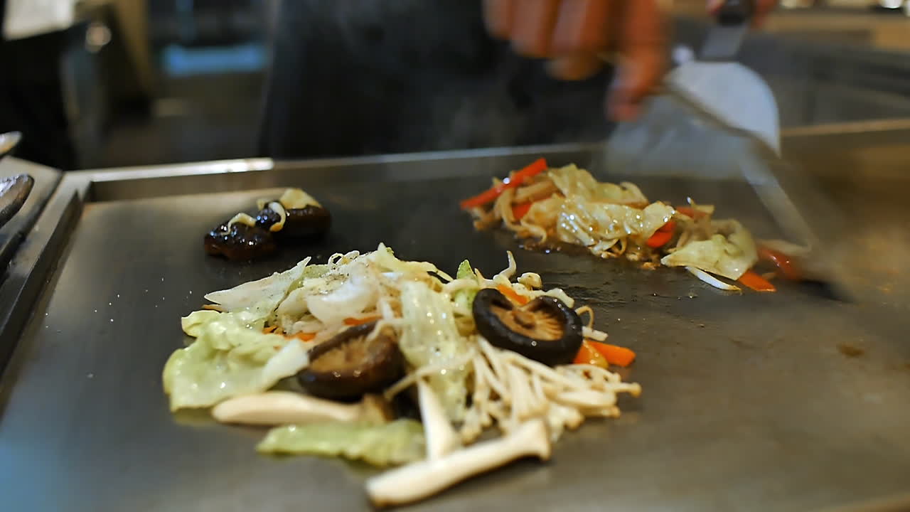 Close-up of a skilled chef preparing teppanyaki Japanese cuisine on a hot iron griddle in front of guests, grilling fresh ingredients with flair. Perfect for Japanese food culture and live cooking
