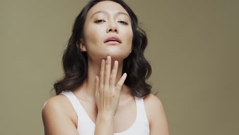 Asiatische-Frau-Mit-Dunklem-Haar,-Die-Ihr-Gesicht-Auf-Beigem-Hintergrund-Mit-Kopierraum-Berührt,-Zeitlupe