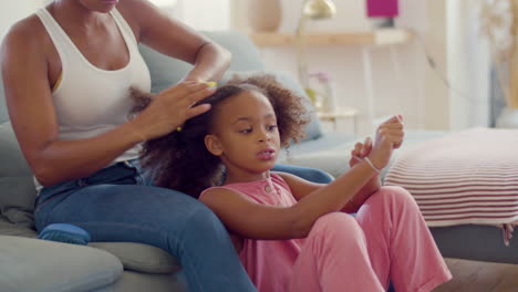 african american mum tying up her little daughter's into pigtails at home