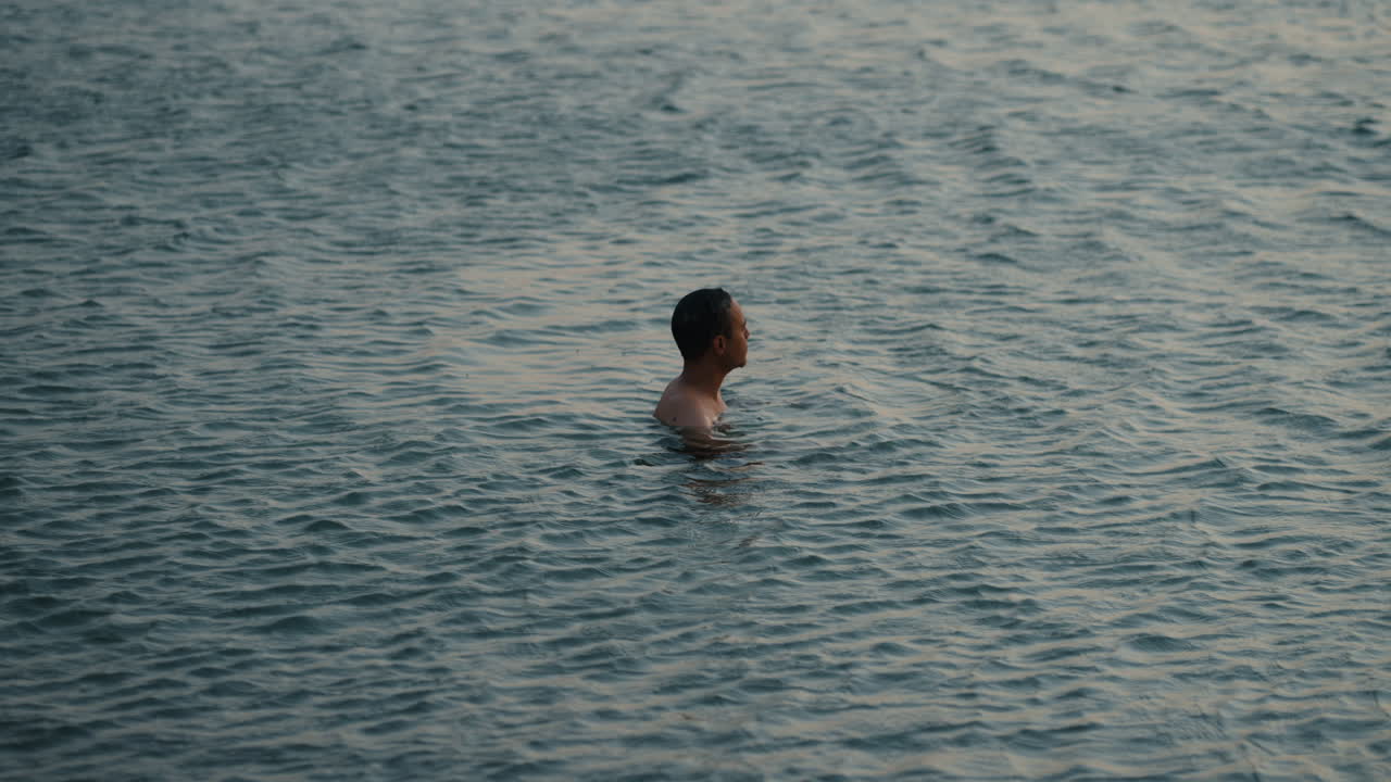 Man swimming in calm sea at blue hour in Sicily, minimal static shot, gazing toward horizon at sunset, serene summer moment
