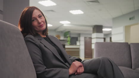 businesswoman sitting in modern office lounge, smiling confidently while relaxing in professional attire. female executive in corporate office looking relaxed and approachable in a calm workspace