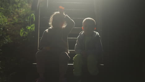 children sitting on cottage stairs silhouettes at night. little boy and girl rest on steps at rural house. kids enjoys warm evening together