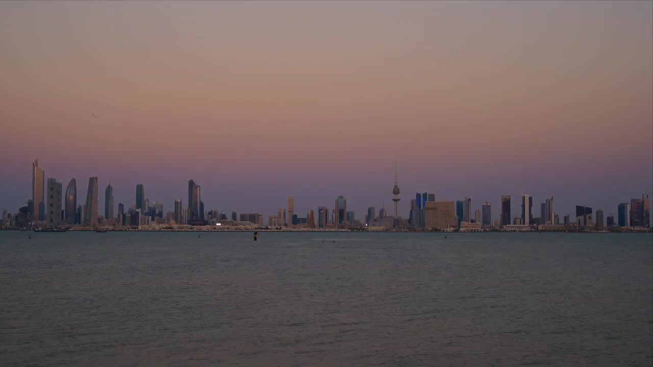 The Kuwait City skyline rises across calm water at dusk, its towers silhouetted against the fading sky in this cinematic cityscape.