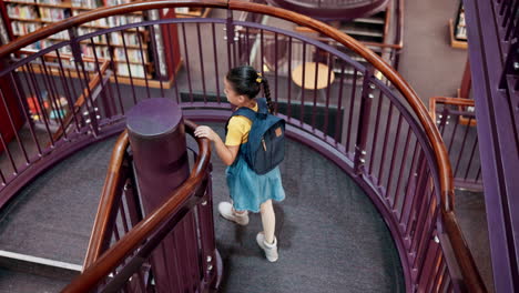 child walking up spiral stairs in library
