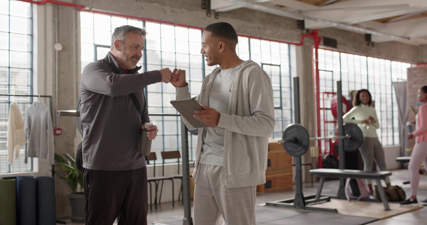 Afrikanischer männlicher Trainer und Kunde im Loft-Fitnessstudio tippt auf Tablet, was zu Nicken führt, Faustgruß, Planbesprechung