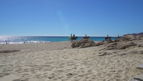 people riding horses on the beach next to water and boulders