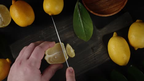 male hands slicing fresh lemon on wooden cutting board.