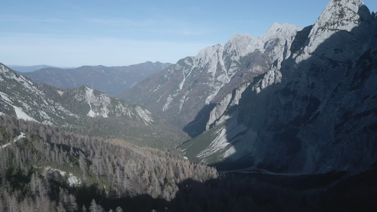 Drone view of Mangart Mountains, Slovenia: jagged peaks, rugged cliffs, lush green valleys, winding alpine roads, dramatic landscape, clear skies, Julian Alps, untouched natural beauty