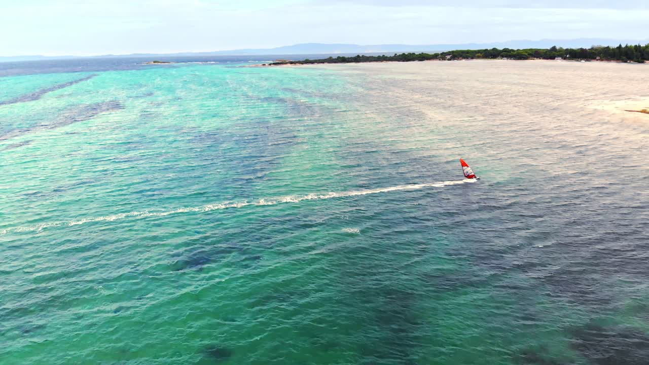 Aerial drone view of a man at windsurfing in Aegean sea. Transparent water, land with greenery in Greece