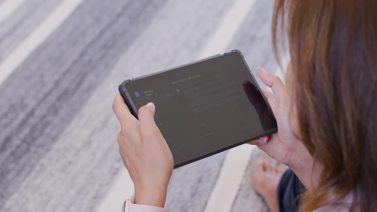 Afroamerikansk kvinne vipper nettbrett i etui mens hun sitter på et stripete teppe, trykker og leser en app