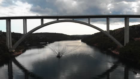 barco de vela siguiendo la cámara bajo un puente de coche en un fiordo en croacia