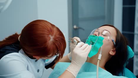 orthodontic procedure. female patient in safety goggles sitting in dental chair during tooth treatment. professional stomatologist treats woman's teeth in dental office.