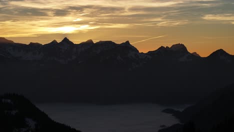 dusk settles over the amden mountains in glarus, silhouettes against the fiery sky, serene and majestic, wide shot