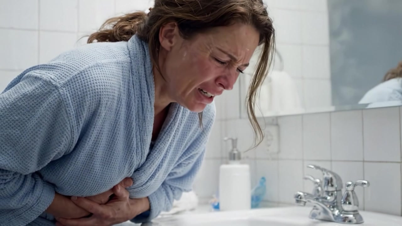 A woman experiencing intense abdominal pain in a bathroom settings, showcasing the emotional and physical distress associated with sudden health crises.