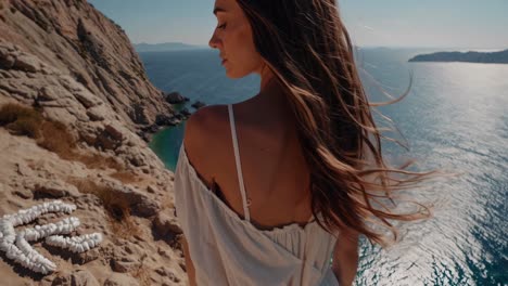 woman wearing white dress standing on rocky cliff overlooking turquoise aegean sea with heart shaped rock formations below, experiencing serene coastal landscape