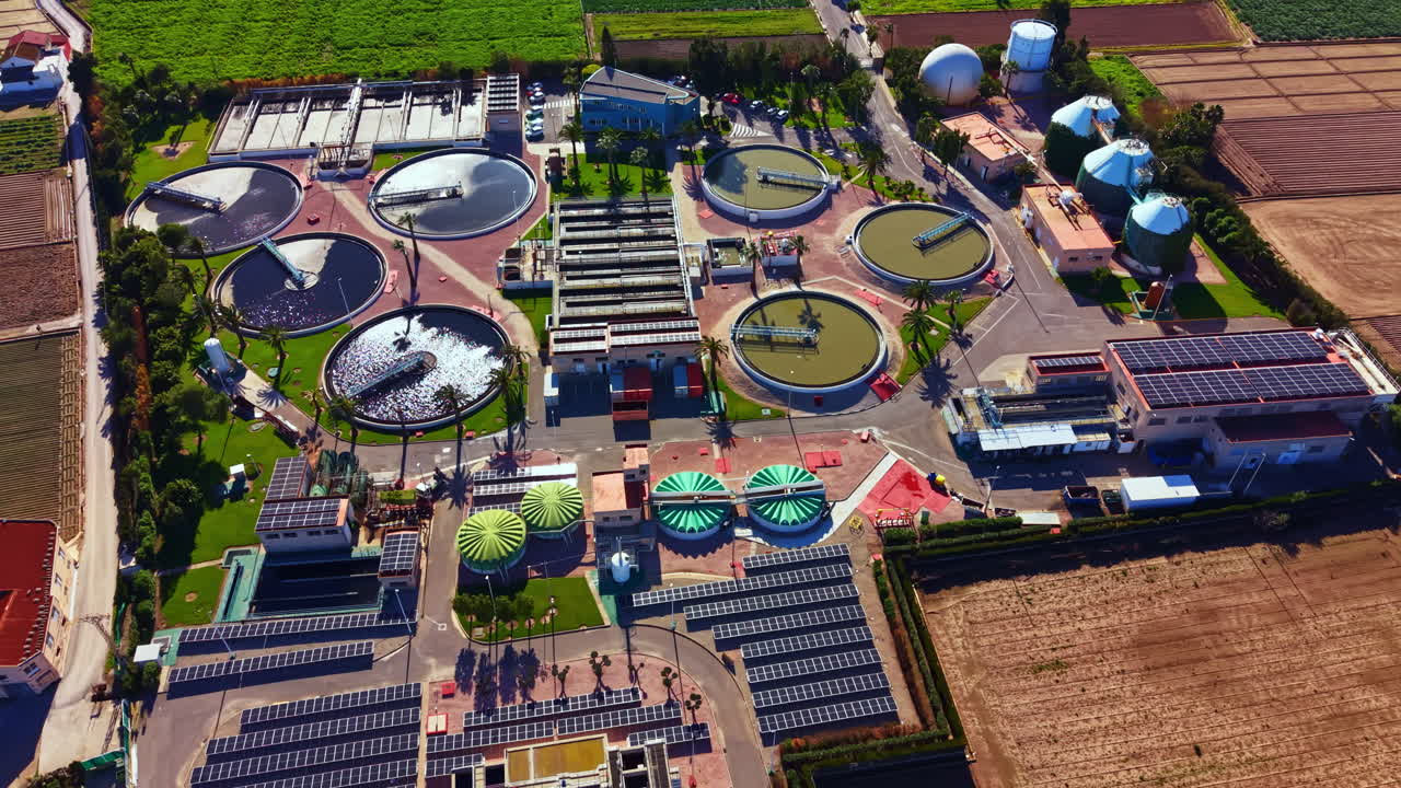 Solar-powered water treatment plant located in a rural area with various tanks and fields during midday