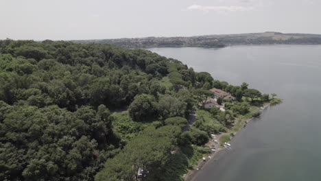 drone shot flying near the edge of the trees at lago di bracciano italy on a bright and sunny day with cars driving on the road near the coastline of the lake log