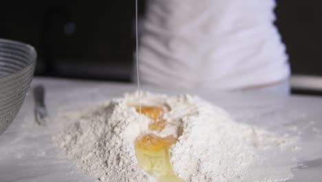 close up view of female hands breaking the second egg into flour on the kitchen table. slow motion shot