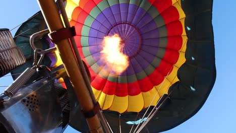 flames from a burner heat the air keeping a brightly colored hot air balloon aloft on a sunny california morning