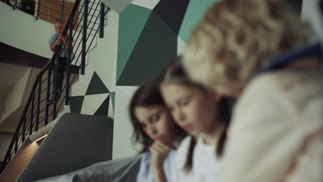 Children-sitting-school-corridor-playing-tablet-closeup.-Boy-standing-stairs.