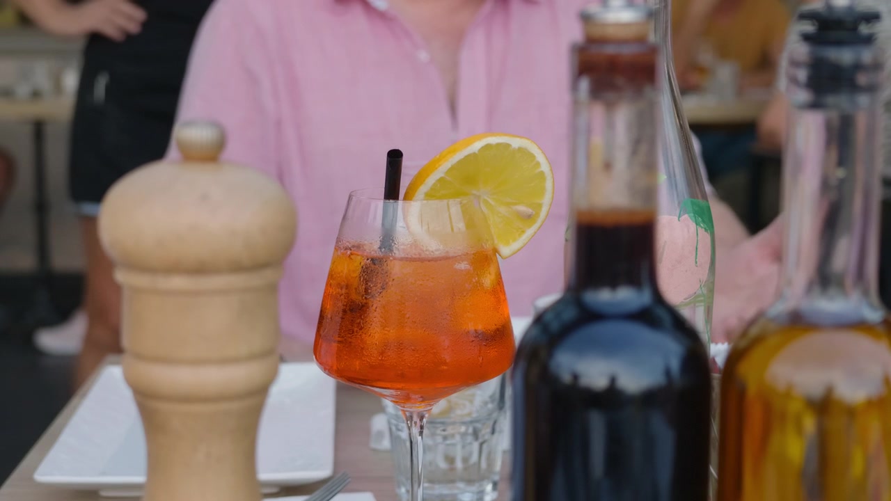 Un cocktail spritz su un tavolo con un macinapepe, bottiglie di olio e aceto.