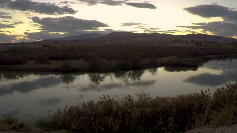 lapso de tiempo de una puesta de sol que se refleja en la superficie lisa de un río y luego se aleja para revelar una escena de gran angular