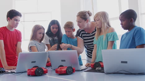 students with female teacher in after school computer coding class learning to program robot vehicle