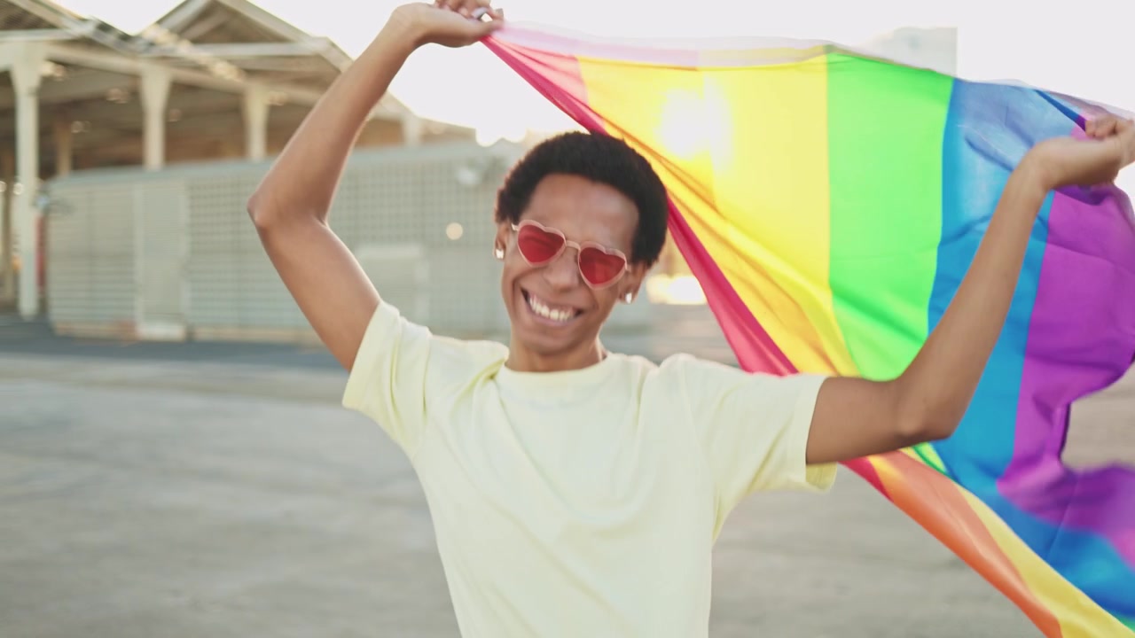 Giovane felice che sventola la bandiera del Pride arcobaleno all'aperto