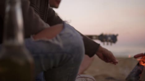 group of young friends sitting by the fire on the beach, grilling sausages and playing guitar. slow motion shot