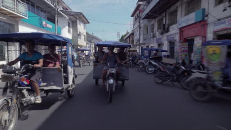 trike taxis drive down a busy street on a sunny day. onboard, rear facing camera. wide shot.
