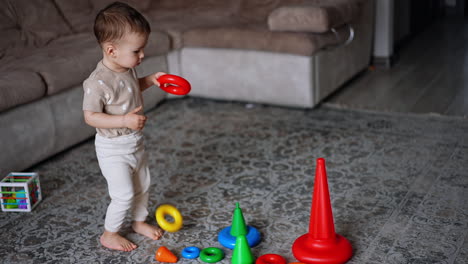 lovely baby boy takes a ring from pyramid. smart toddler assembling the toy in the room.