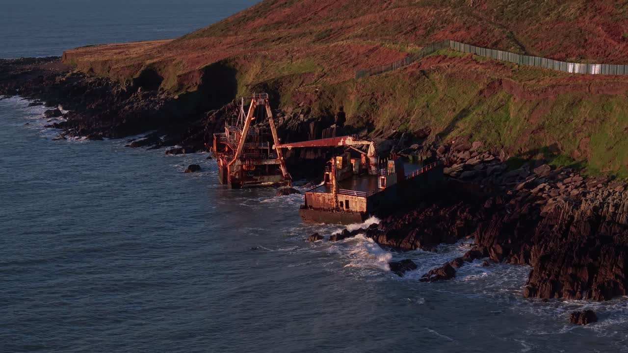 A fishing boat wreck rests on rocky shores under golden hour light, Ballycotton, Cork