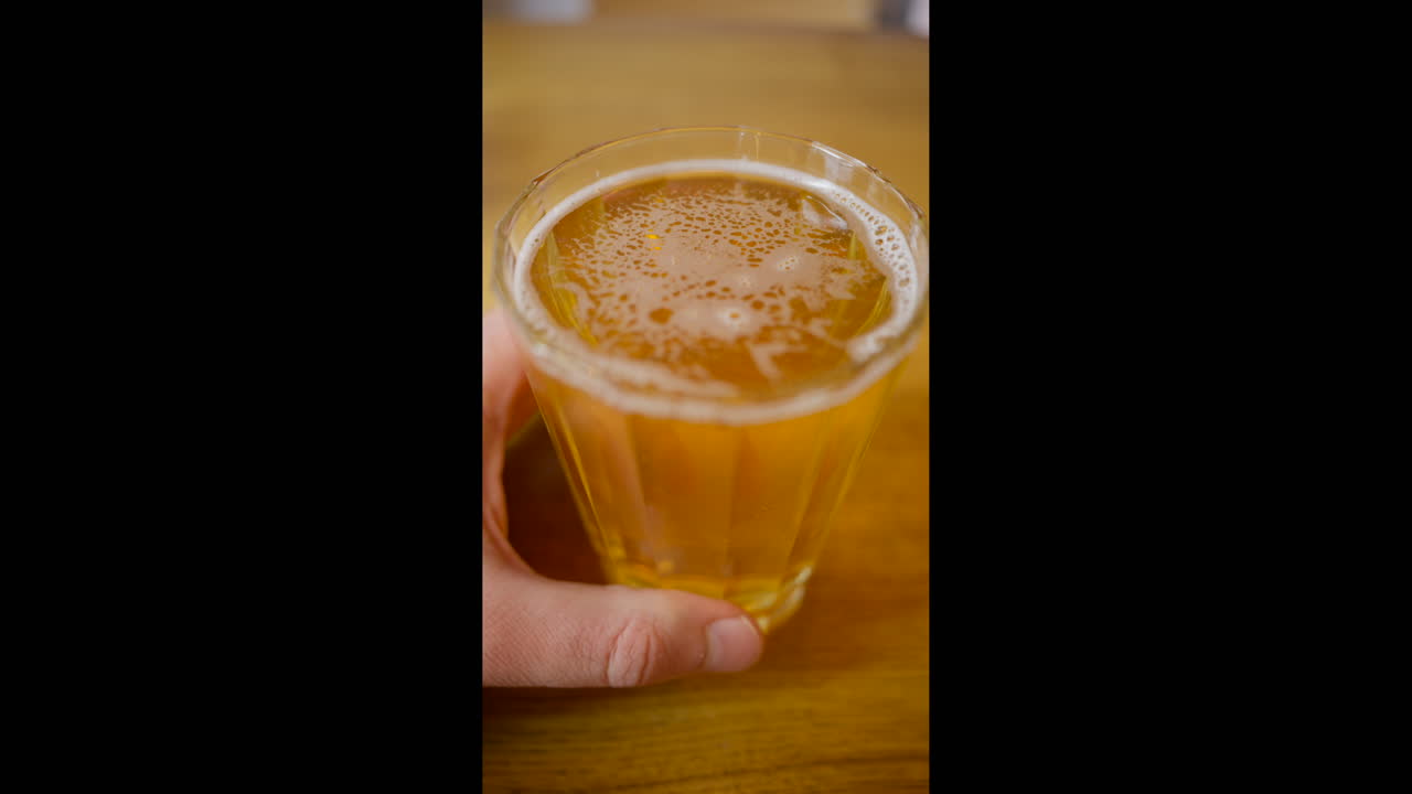 Ahşap bir masada, köpüklü, yeni doldurulmuş açık renkli lager bira bardağının üstten görünümü. Dikey.